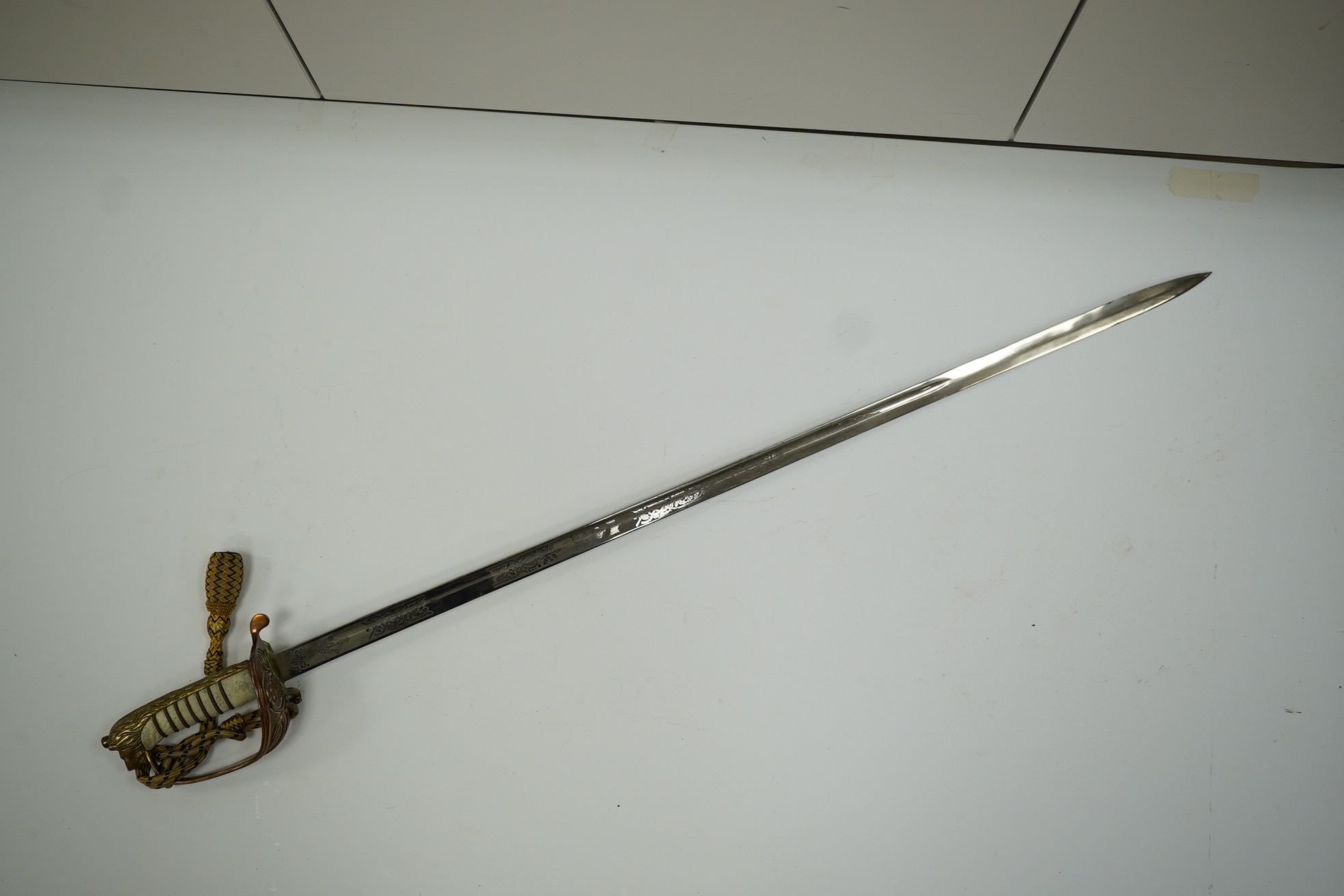 An 1846 pattern naval officer’s sword by Gieves, with folding thumb guard and knot, in its leather scabbard with brass mounts. Together with its outer soft leather cover. Condition - fair, notable wear to grip.